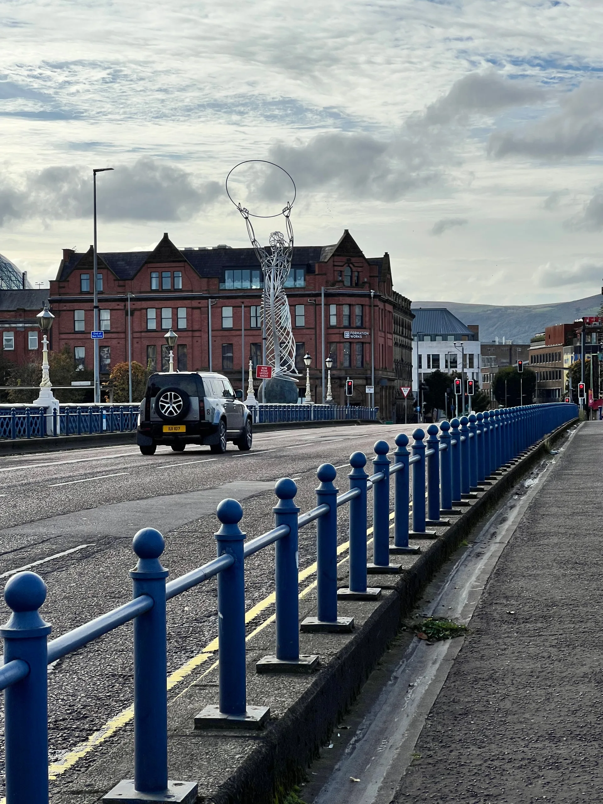Blue railings along Queen's Bridge, the Beacon of Hope sculpture beyond.