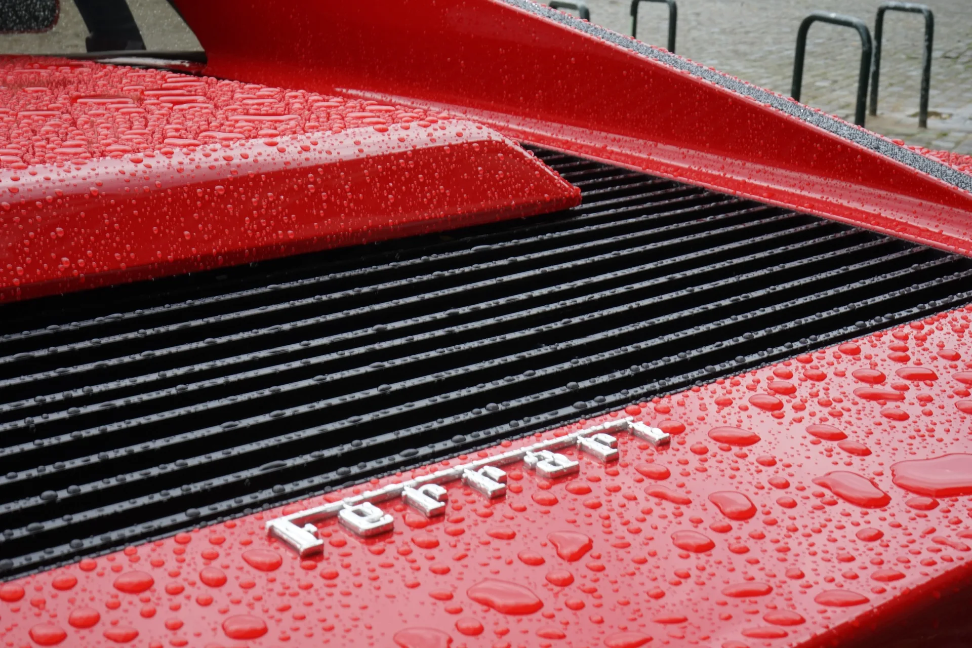 The Ferrari script on a wet red engine cover, rain beaded on the paint.