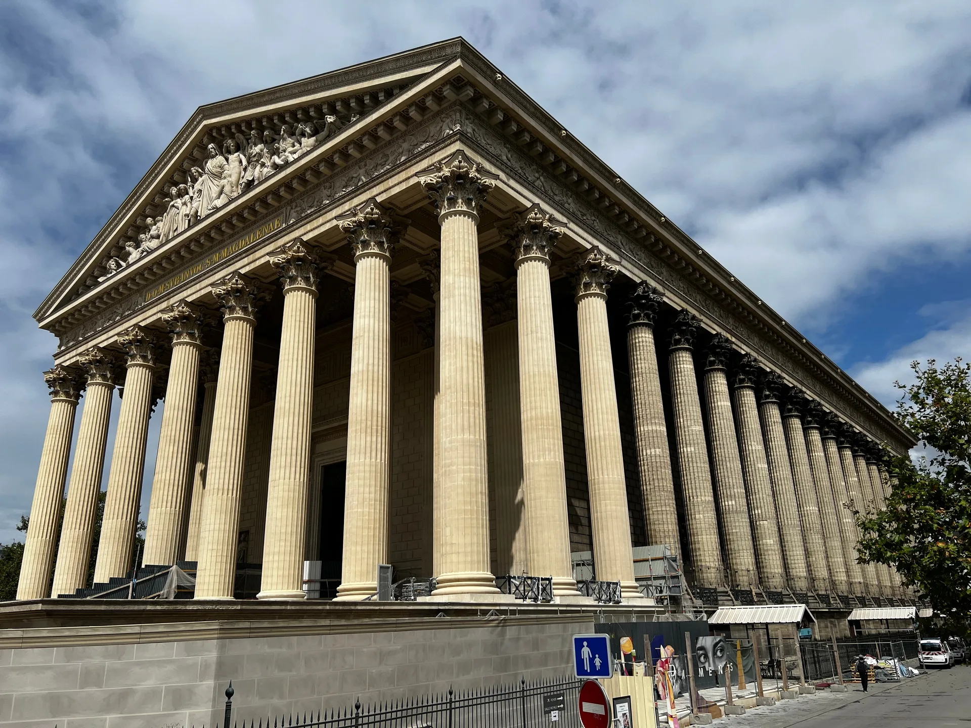 The colonnade of La Madeleine against a clouded sky, seen from the street below.