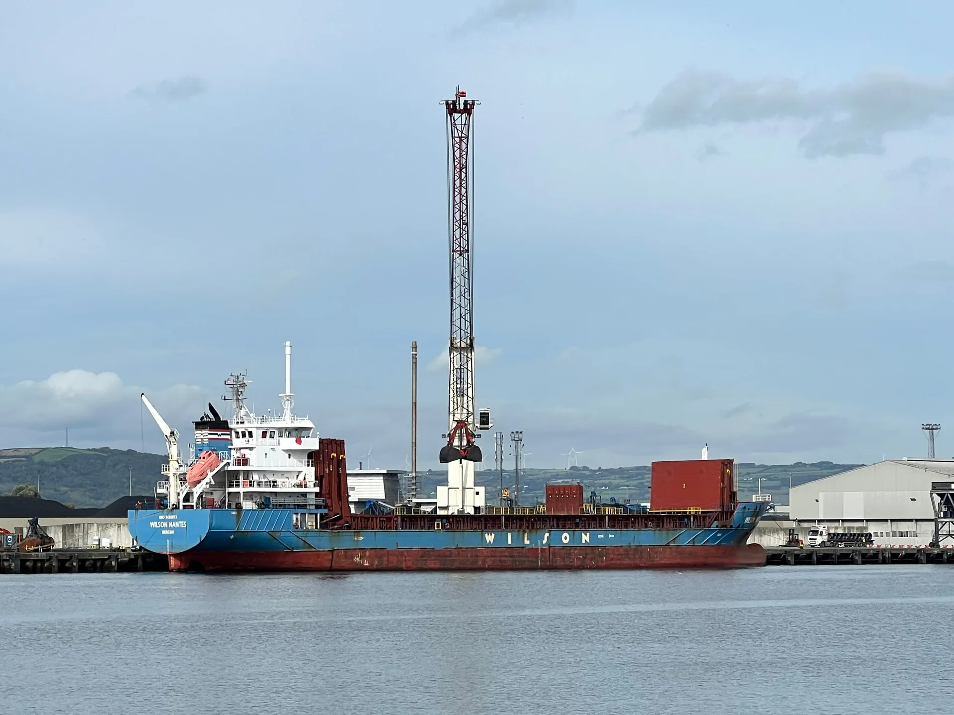 A cargo ship alongside a quay in Belfast harbour, a crane behind it.