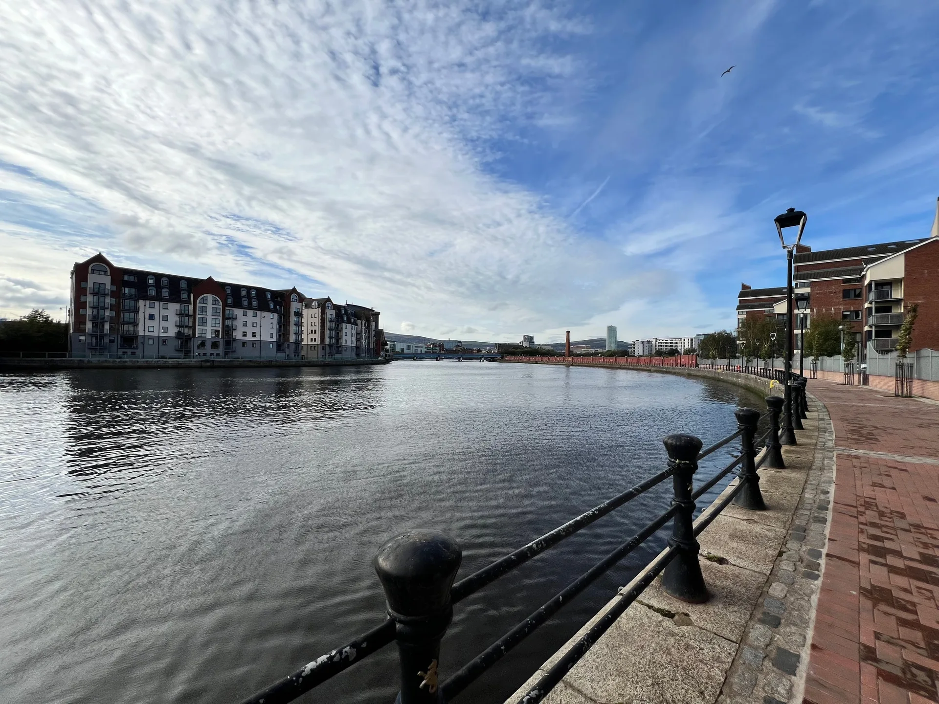 The River Lagan under a broken sky, black railings along the quay and apartment blocks on the far bank.
