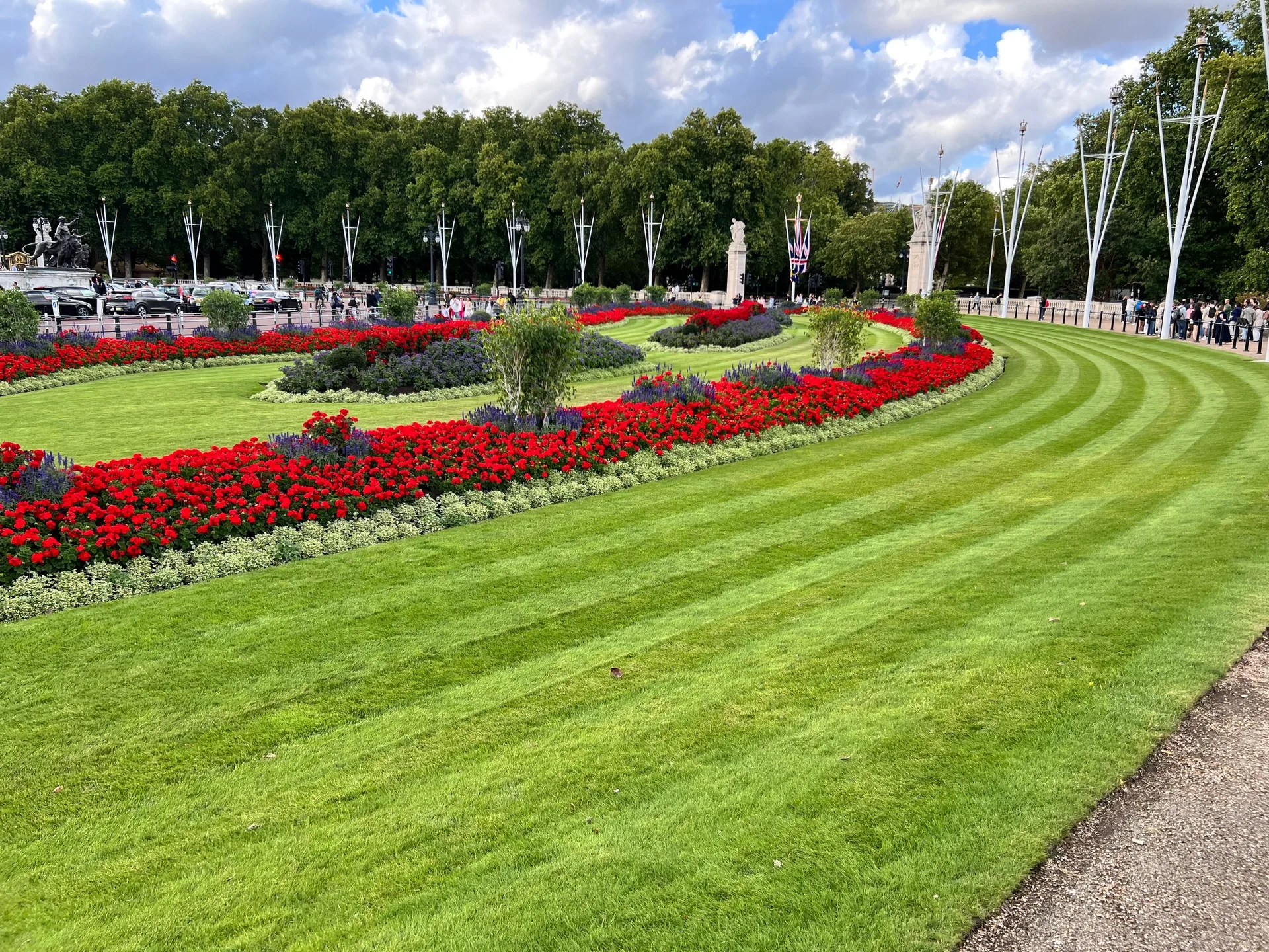 Red flower beds and striped lawns below Buckingham Palace, flags along the Mall.