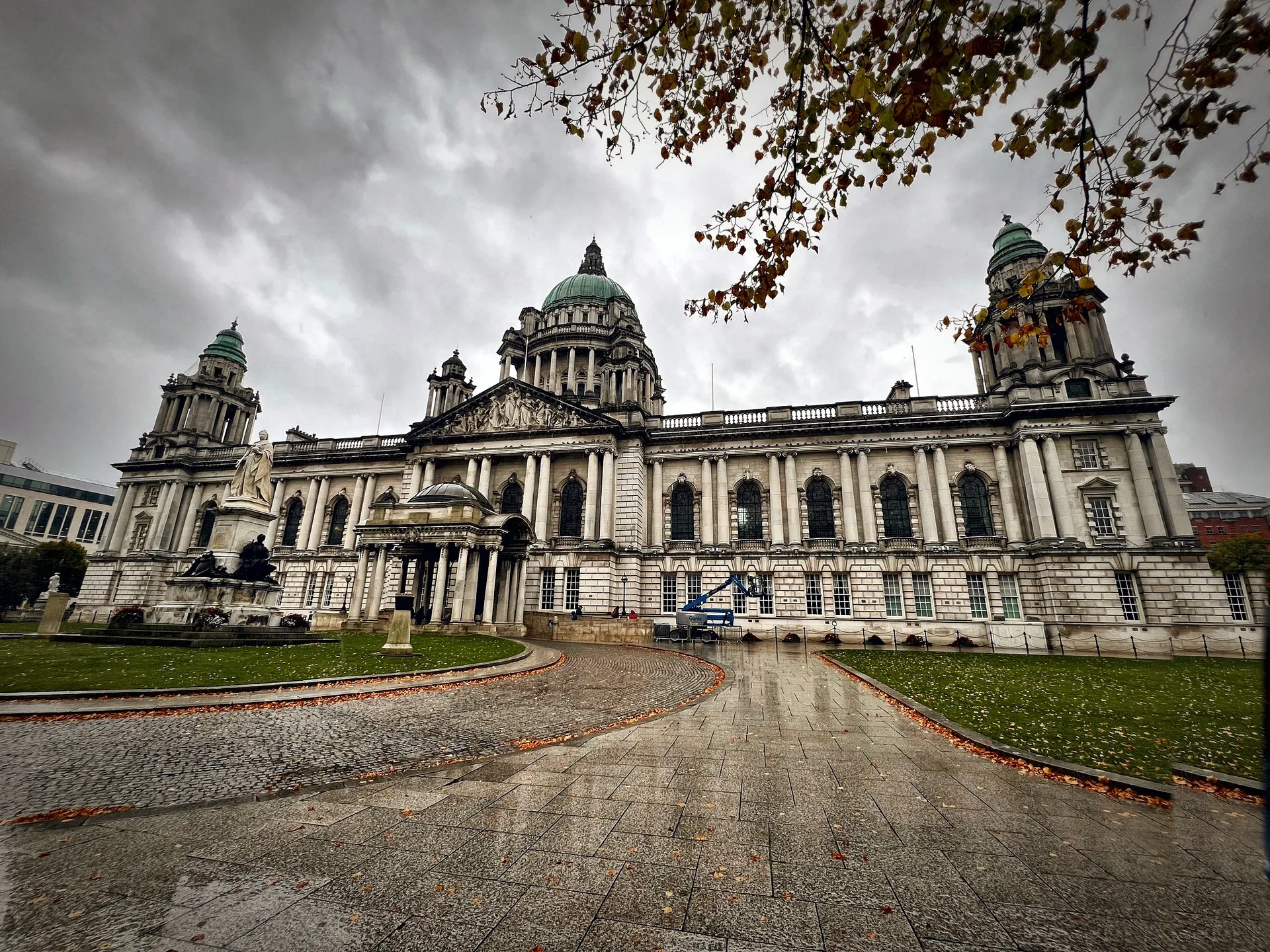 Belfast City Hall under an autumn sky, a tree branch in the foreground.