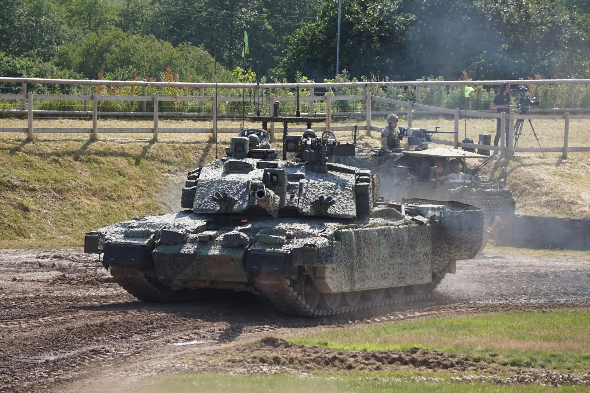 A Challenger 2 tank crossing a muddy arena, its tracks throwing up earth.